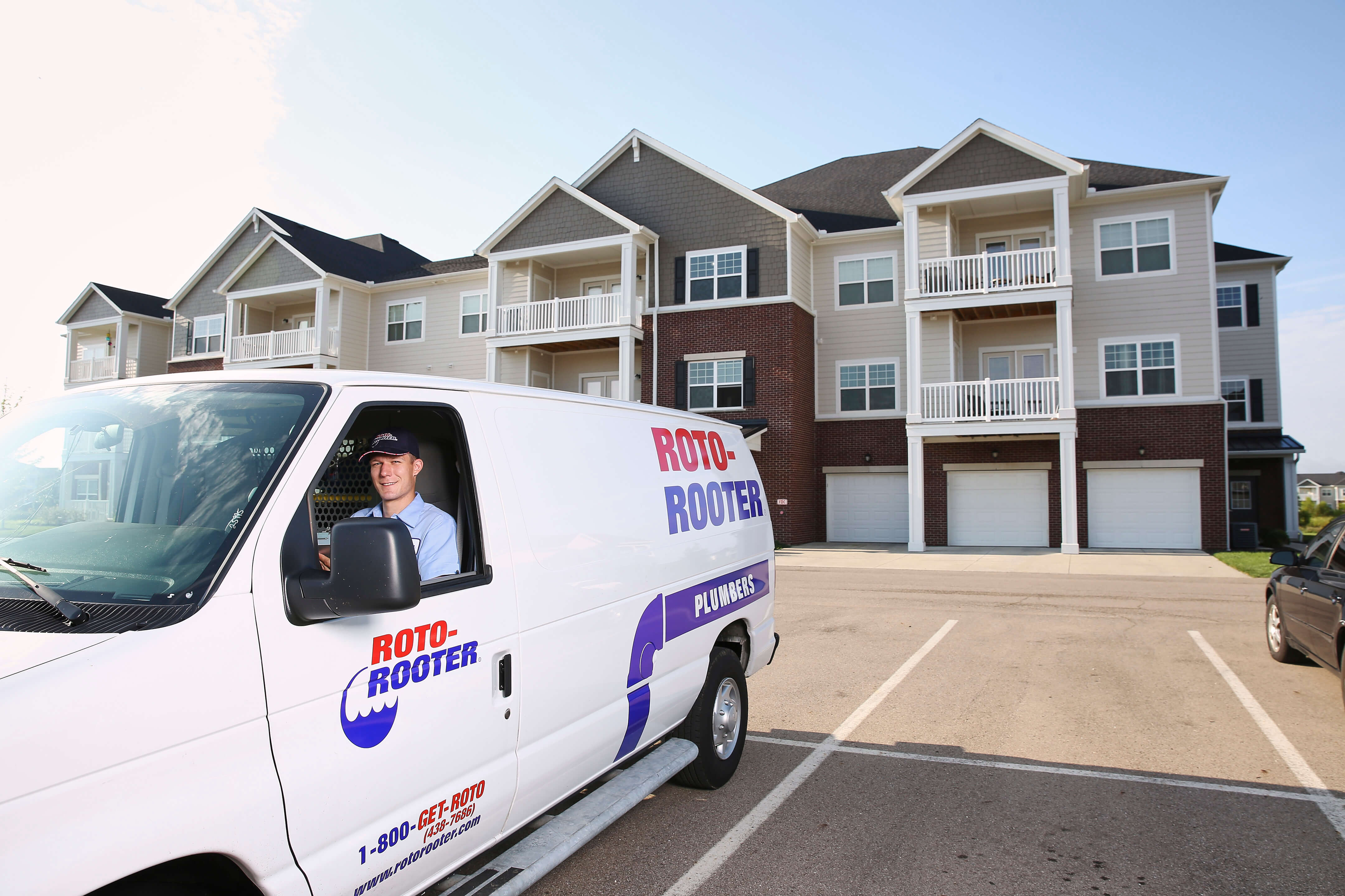 Roto-Rooter plumber sitting in company-branded van parked outside apartment building