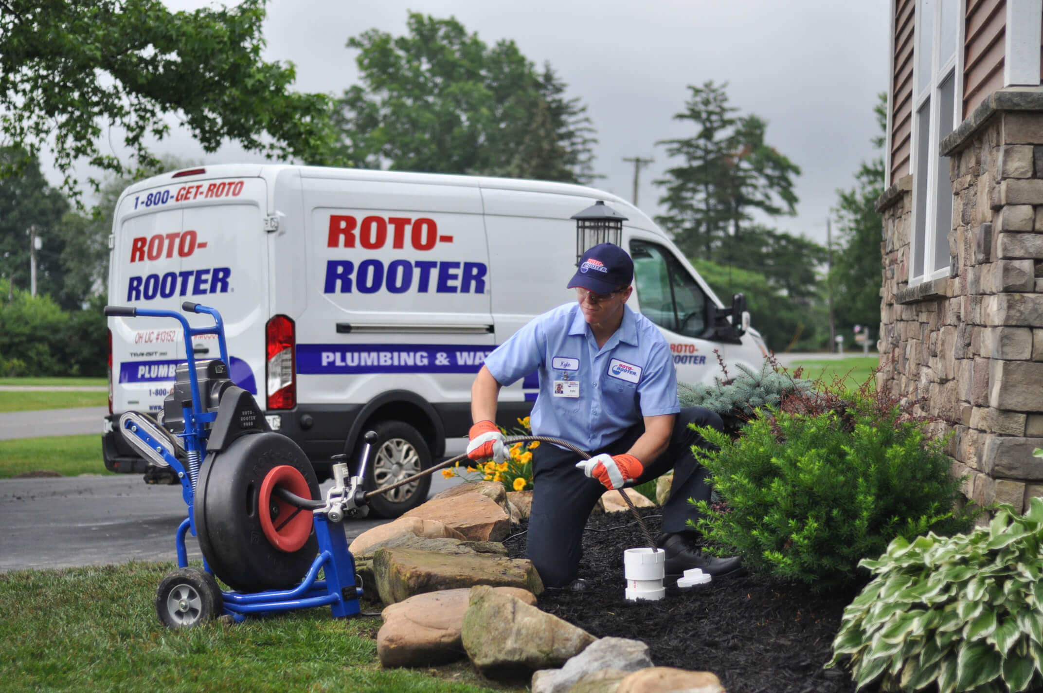 Plumber in customer's front yard using drain cleaning machine to perform sewer line cleaning