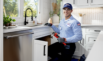 Smiling plumber holding wrench, working on garbage disposal